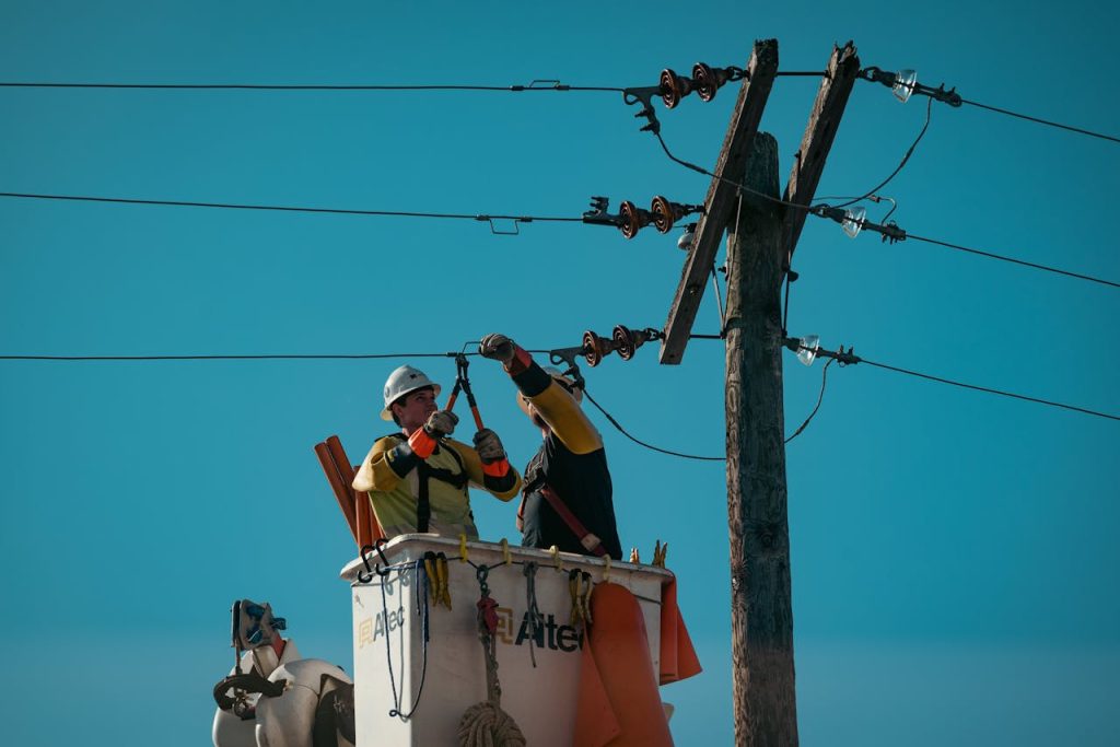 Electricians in safety gear working on power lines in bright daylight. Energy industry focus.